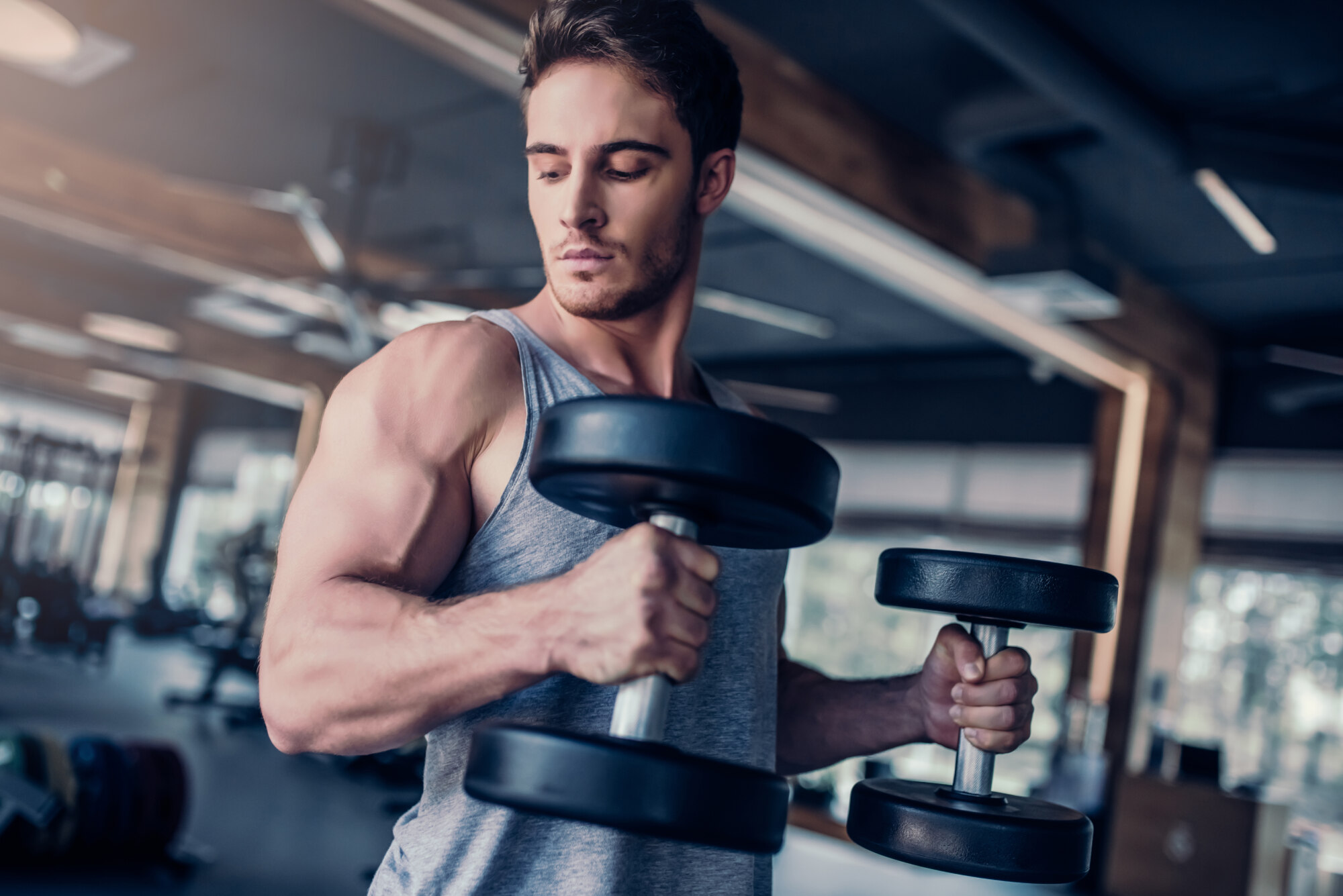 Handsome muscular man is training in gym. Sports man with dumbbells